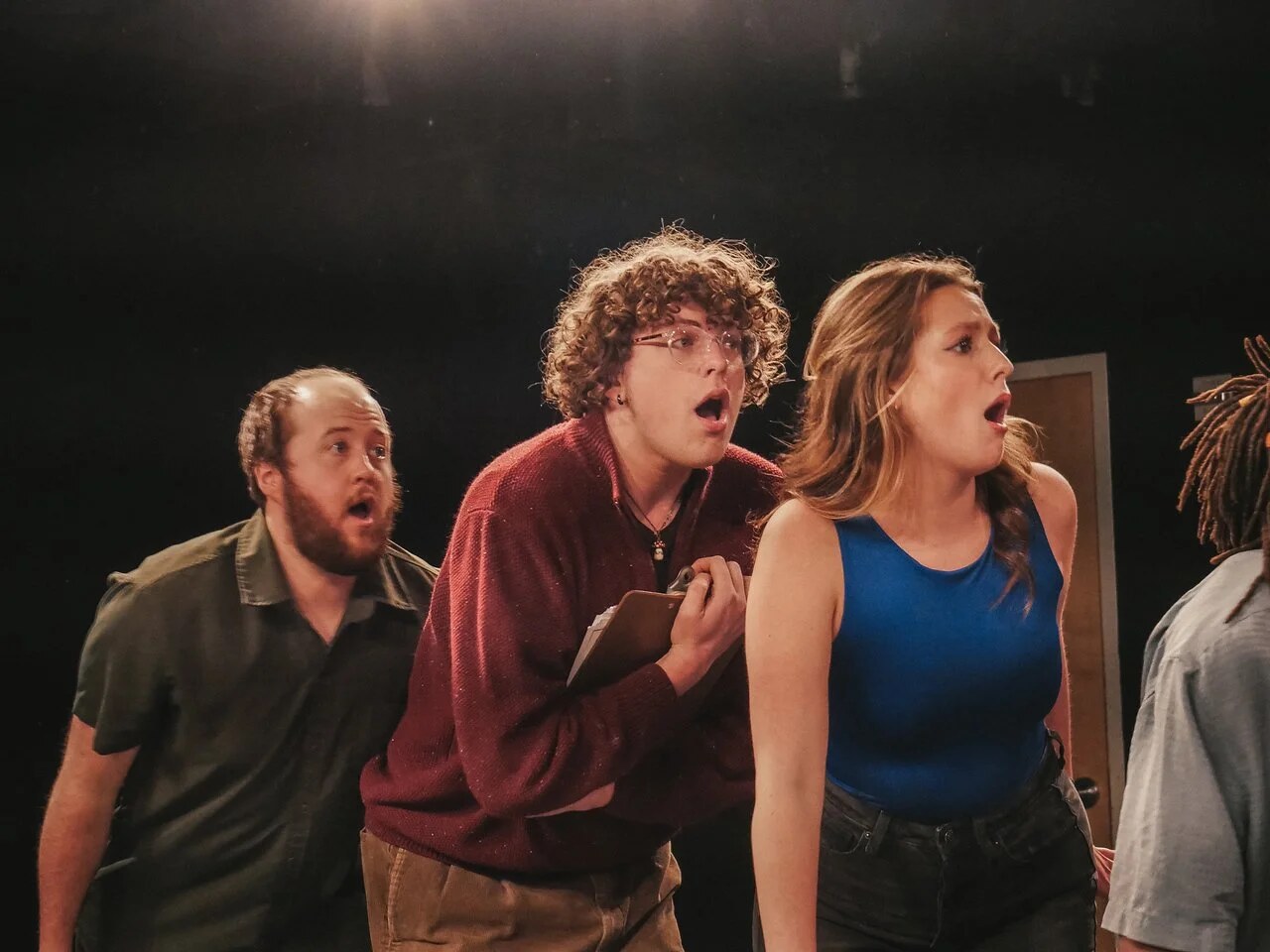 Performers singing together, with the center performer holding a notebook against a burgundy sweater.