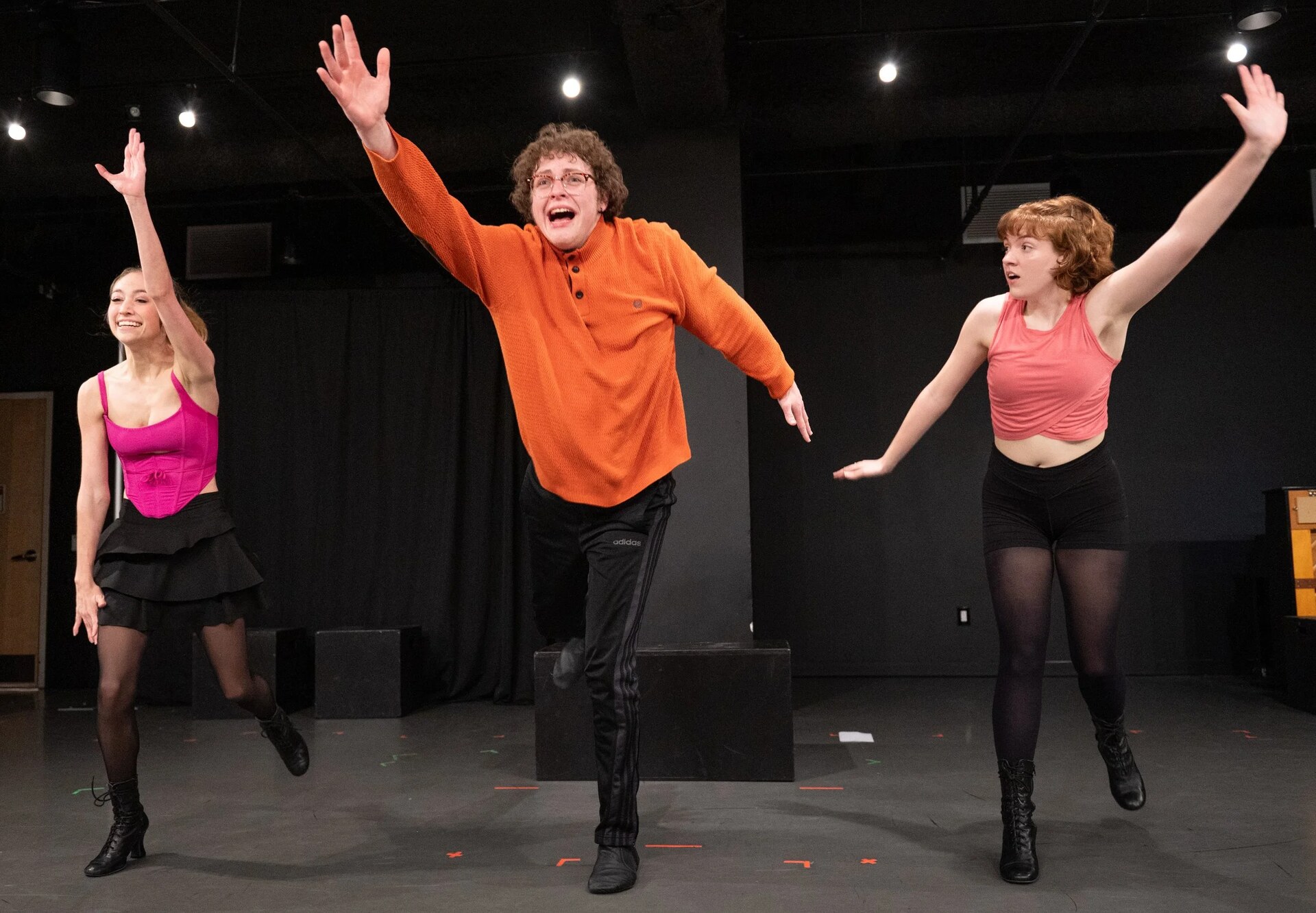 Three performers dancing with one arm raised, the center performer in an orange sweater.