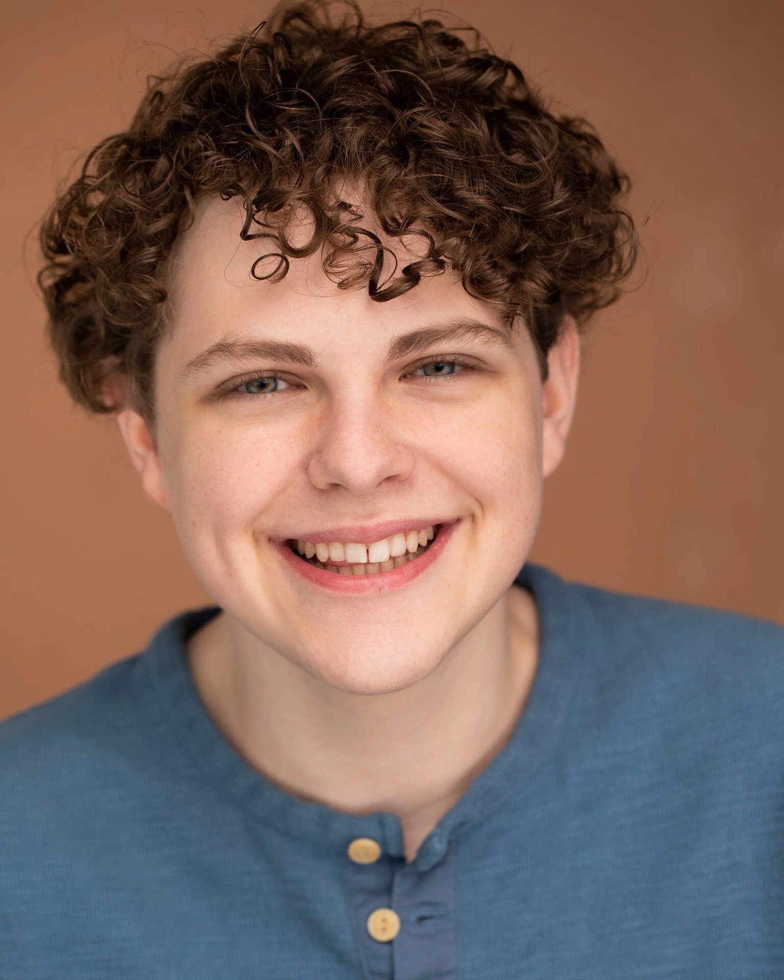 Finn Rutis, smiling in a blue shirt against a warm brown background.